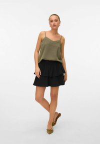 Top sans manches vert olive avec des bretelles fines, associé à une jupe noire à volants. La tenue présente une texture douce et une coupe décontractée.