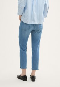 Gaisblue straight leg džinsi ar izbalējušu apdari, kroptām potītēm un piecu kabatu dizainu, saskaņoti ar zilu un baltu svītru krekli.