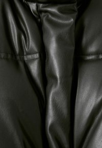 Černá kožená látka s hladkou strukturou, vybavená měkkými záhyby a prošitými detaily, vytvářející vrstvený vzhled.