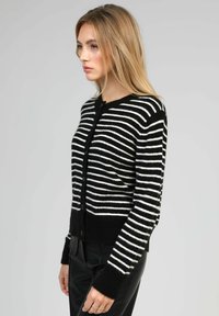 Cardigan rayé noir et blanc avec une texture douce, col rond, boutons sur le devant, et poignets et ourlet côtelés.