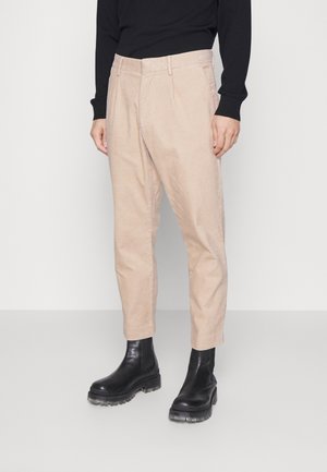 Homme portant un pantalon beige en velours côtelé fuselé, un haut noir à manches longues et des bottines en cuir noir épaisses.