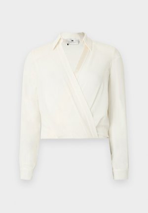 Blusa corta a maniche lunghe in tessuto color avorio. Presenta un design avvolgente con collo classico e polsini con bottoni. Texture liscia, dettagli minimali.