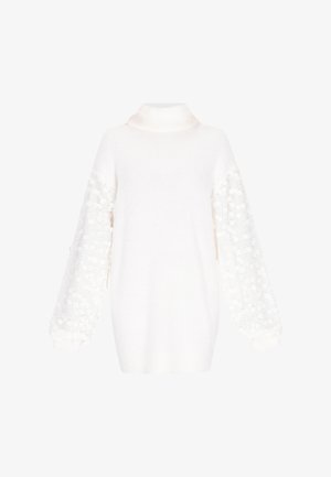 Fehér kötött pulóver magas gallérral és voluminózus, mintás ujjakkal, amelyek texturált pöttyökkel és bordázott mandzsettákkal díszítettek.