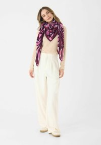 Sciarpa leggera e patterned in un profondo rosa e viola, con un design geometrico. Indossata sopra una maglietta beige con pantaloni larghi color crema.