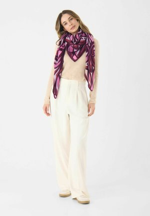 Écharpe légère à motifs en rose foncé et violet, arborant un design géométrique. Portée drapée sur un haut beige avec un pantalon large couleur crème.