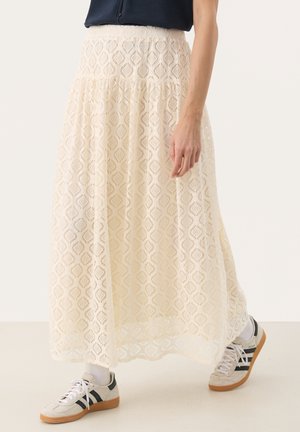 Lång spetskjol i off-white med ett diamantmönster, med en lagerpåläggningsdesign och resårmidja, kombinerad med sneakers.