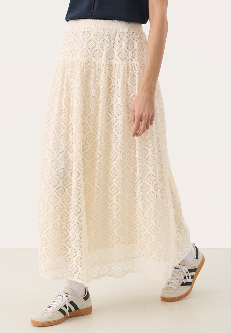 Jupe maxi en dentelle blanc cassé avec un motif en losange, présentant un design à volants et une taille élastique, associée à des baskets.