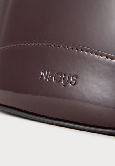 Chaussure en cuir marron poli avec coutures visibles et le nom de la marque Neous embossé sur le côté près de la semelle.