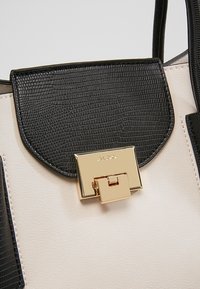 Svart och krämfärgad handväska med en texturerad, konstläderkropp, en slät klaff och ett guldtonat spänne med en rektangulär design.