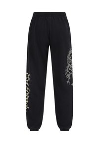 Svarta träningsbyxor med en avslappnad passform, som har ett elastiskt midjeband, smalnande muddar och en stor silverfärgad tiger-grafik på vänster ben.