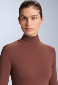 Brun, långärmad polo i slät, stretchig tyg. Designen har en figurnära silhuett och hög hals.