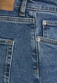 Jeans in denim blu con tasca frontale, cuciture in rame e rivetti metallici. La texture è leggermente sbiadita con un design a vestibilità classica.