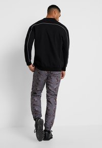 Melna sporta kreklu ar baltām akcentējošām šuvēm un pelēkas bikses ar kamuflāžas rakstu. Biksēm ir brūni un balti akcenti, sašaurinātas kāju malas.