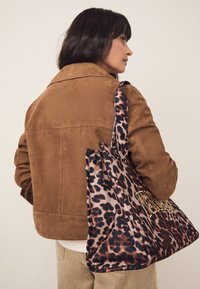 Geantă tip tote cu imprimeu leopard, accente negre și maro, material textil și detaliu mare cu logo auriu. Are forma unei genți hobo moi.