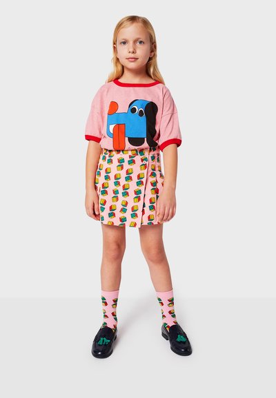 Lyserød T-shirt med et farverigt hundemotiv, parret med en mønstret lyserød nederdel med byggeklodser. Sorte sko og mønstrede sokker fuldender looket.