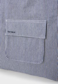Kék és fehér csíkozott textil zsebbel és márkázott címkével. A textúra szőttnek tűnik, és a csíkok egyenletesen vannak elhelyezve.