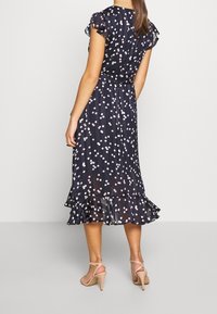 Navy dress with white and pink polka dots, ruffled sleeves, and a flared hem. Made of lightweight fabric, it features a fitted waist.