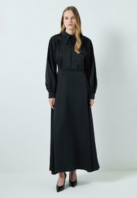 Black long-sleeve dress with a fitted bodice, large collar, and front button closure. Flowing fabric with a smooth texture and full-length design.