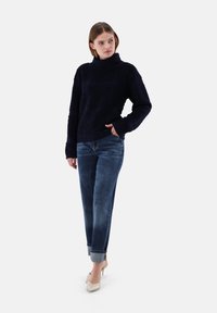 Marineblau strukturierter Rollkragenpullover mit langen Ärmeln, kombiniert mit hellblauen Jeans und beigen High-Heels.