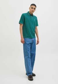 Tricou polo verde cu un model texturat, având guler și accente cu dungi. Asortat cu blugi largi albaștri și pantofi negri.