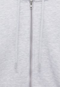 Tissu de sweat à capuche zippé gris clair avec une fermeture éclair argentée centrée et des cordons assortis suspendus de chaque côté.