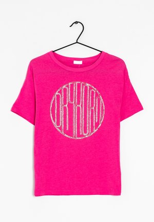 Felroze T-shirt met korte mouwen, met een zilveren glittercirkel en gestileerde letters, hangend aan een zwarte hanger tegen een witte achtergrond.