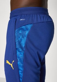 Shorts athletici albaștri, cu un material texturat și un model grafic vibrant albastru pe lateral, cu un logo vizibil și tehnologie de absorbție a umidității.
