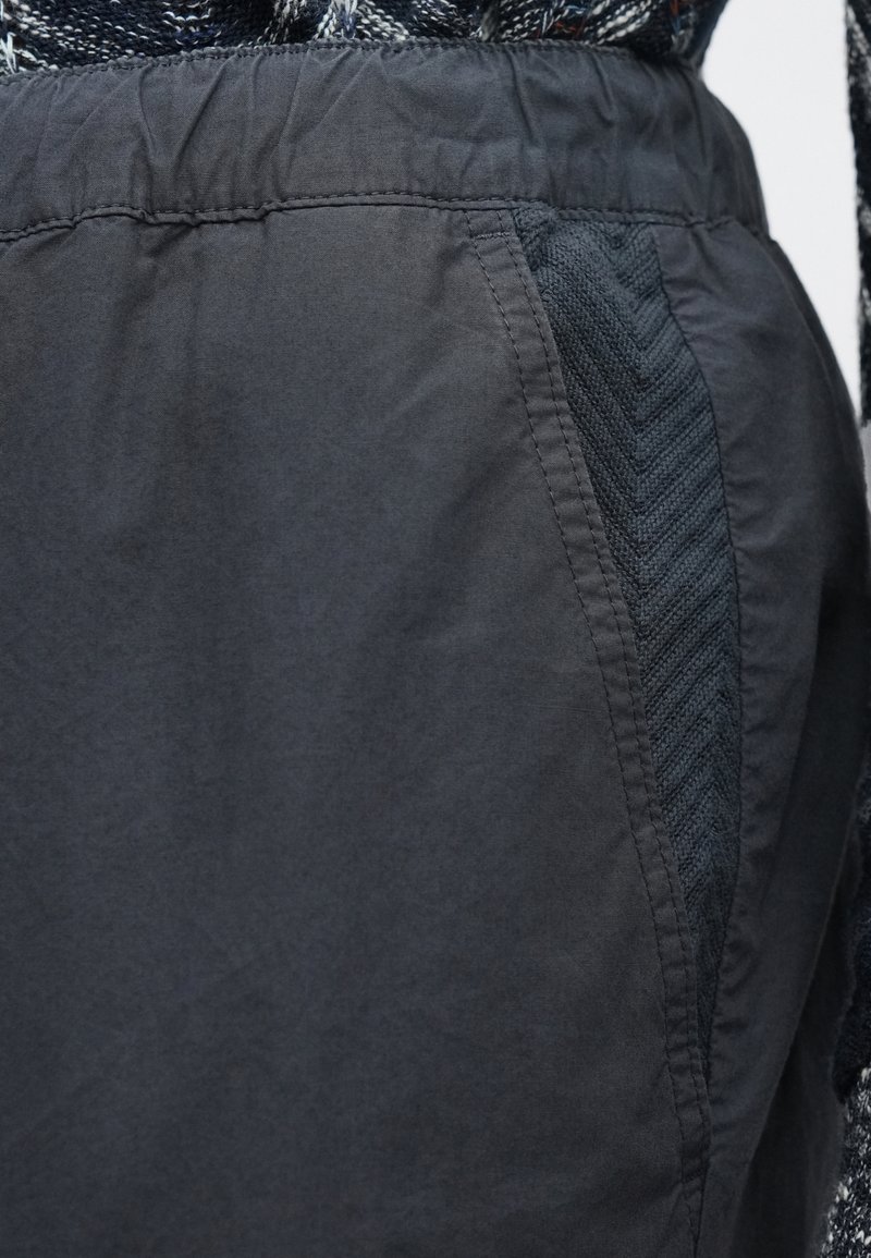 Shorts gris foncé avec une taille élastique, dotés d'un panneau latéral texturé avec un motif en chevrons. Texture de tissu lisse, design décontracté.