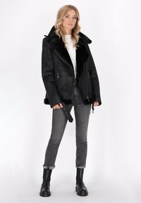 Sort faux læderjakke med en plyskrave, der har lynlåsdetaljer, parret med grå tapered jeans og sorte combat støvler.