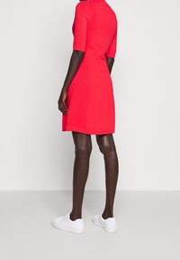 Robe en maille rouge à manches courtes, texture côtelée et silhouette ajustée. Associée à des baskets blanches pour un look décontracté.