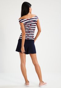 Top bez ramínek s námořnickými a bílými pruhy, květinový vzor; spárováno s námořnickou skort a růžovými skládacími botami. Hladká tkanina, ležérní design.