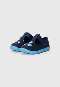 Chaussures en tissu bleu foncé avec une sangle ajustable, présentant une semelle bleu clair. Les détails remarquables incluent le numéro "5" et des accents graphiques liés au football.