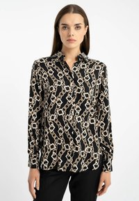 Czarna bluzka z wzorem łańcucha w kolorze złotym i bia�łym. Długie rękawy i kołnierzyk. Gładki materiał z delikatnym połyskiem.