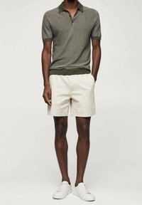 Polo rayé olive à manches courtes, associé à un short beige. Des baskets blanches complètent la tenue. Design simple et décontracté.