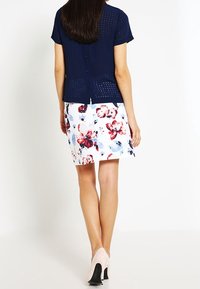 Marinblus med kort ärm och strukturerad mönster, i kombination med en blommig pennkjol i vitt, rosa och blått. Modellen bär beige klackar.