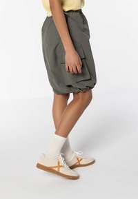 Pantaloni cargo verdi con vita elasticizzata e tasche laterali, abbinati a sneakers crema con accenti arancioni e calze bianche a coste.