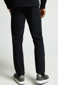 Zwarte tapering broek met platte zakken en een rekbare tailleband. Gecombineerd met grijze sneakers en een gestructureerd zwart shirt.