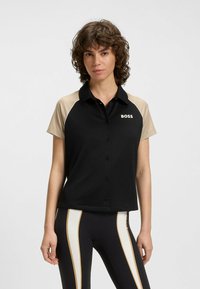 Svart kortärmad polo med beige axlar, framknappar och "BOSS"-logotyp. Mjuk tygkvalitet med en skräddarsydd passform.