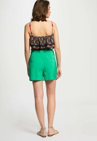 Shorts verdi a vita alta con taglio dritto, abbinati a un top corto nero con fiori, caratterizzato da ruffle e spalline decorate.