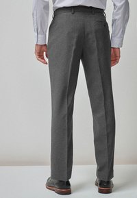 Pantalon en laine gris avec une coupe droite, doté d'un petit détail de poche et porté avec des chaussures noires et une chemise à motifs.