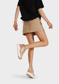 Sneakers sportivi beige con pannelli in rete, dettagli dorati e suola bianca. Abbinati a una maglietta nera e una gonna in suede beige.