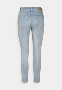 Jeans ajustados de color azul claro hechos de mezclilla, con una cintura alta, diseño de cinco bolsillos y un ligero desgaste. La vista trasera muestra la etiqueta en la cinturilla.