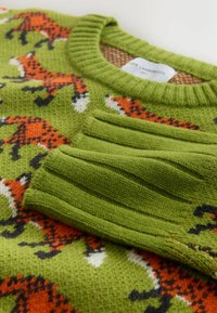 Zöld kötött pulóver narancssárga és fekete róka mintával, bordás nyakkal és mandzsettákkal, puha, textúrált fonalból készült.