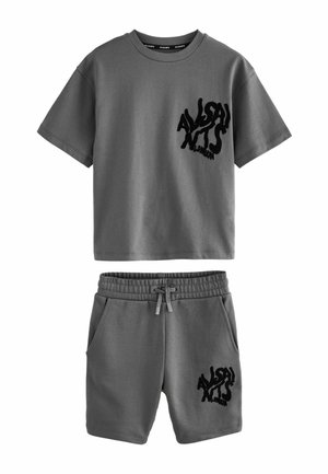 Camiseta de algodón gris de manga corta y shorts a juego, con un logo negro texturizado en el pecho izquierdo y el muslo, y cintura elástica.