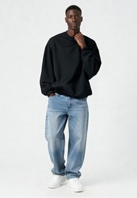 Felpa nera con spalle scese, jeans larghi azzurri chiaro e sneakers bianche. Design semplice, tessuto di peso medio e vestibilità rilassata.