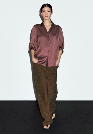 Chemise boutonnière en satin mauve avec col et manches retroussées, associée à un pantalon en daim marron taille haute. Coupe simple et décontractée.