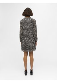 Robe noire à fleurs avec des manches longues, taille froncée et jupe à layers. Le matériau semble léger et semi-transparent avec de petits motifs floraux.