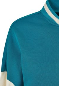 Zbliżenie na turkusową i białą koszulę z długim rękawem, z prążkowanym kołnierzykiem, który ma turkusowe i białe paski.