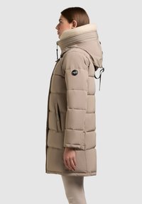 Beige péřová bunda s vysokým límcem a fleecovou podšívkou, s prošívaným designem, zipovými kapsami a logem na rukávu.