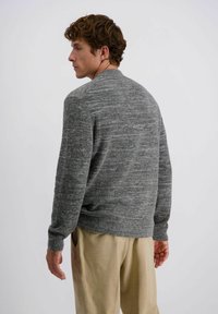Grijze gebreide trui met een gestructureerde afwerking, ronde halslijn en geribde manchetten. In combinatie met beige broeken, wat een casual pasvorm laat zien.
